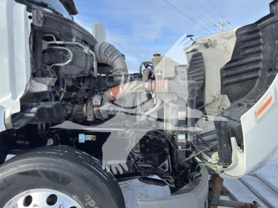 Peterbilt 579 engine bay with visible intake hoses, coolant reservoir, and front wheel; shows engine components and cab opening.