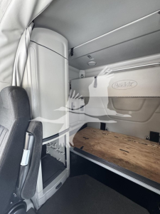 Peterbilt 579 interior sleeper cab with wooden bed platform, side storage panel, and logo reading Peterbilt. Cabin area shows side wall panels and overhead compartments.