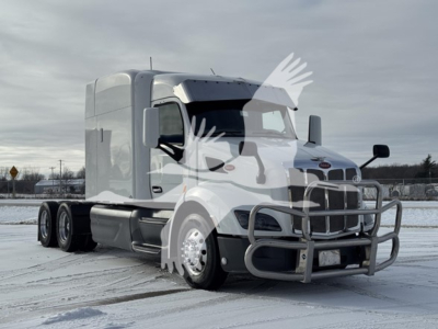 Peterbilt 579 tractor in snowy lot, silver cab, chrome bumper guard, dual rear wheels, manufacturer badges visible on grille, no visible text legible other than truck design.