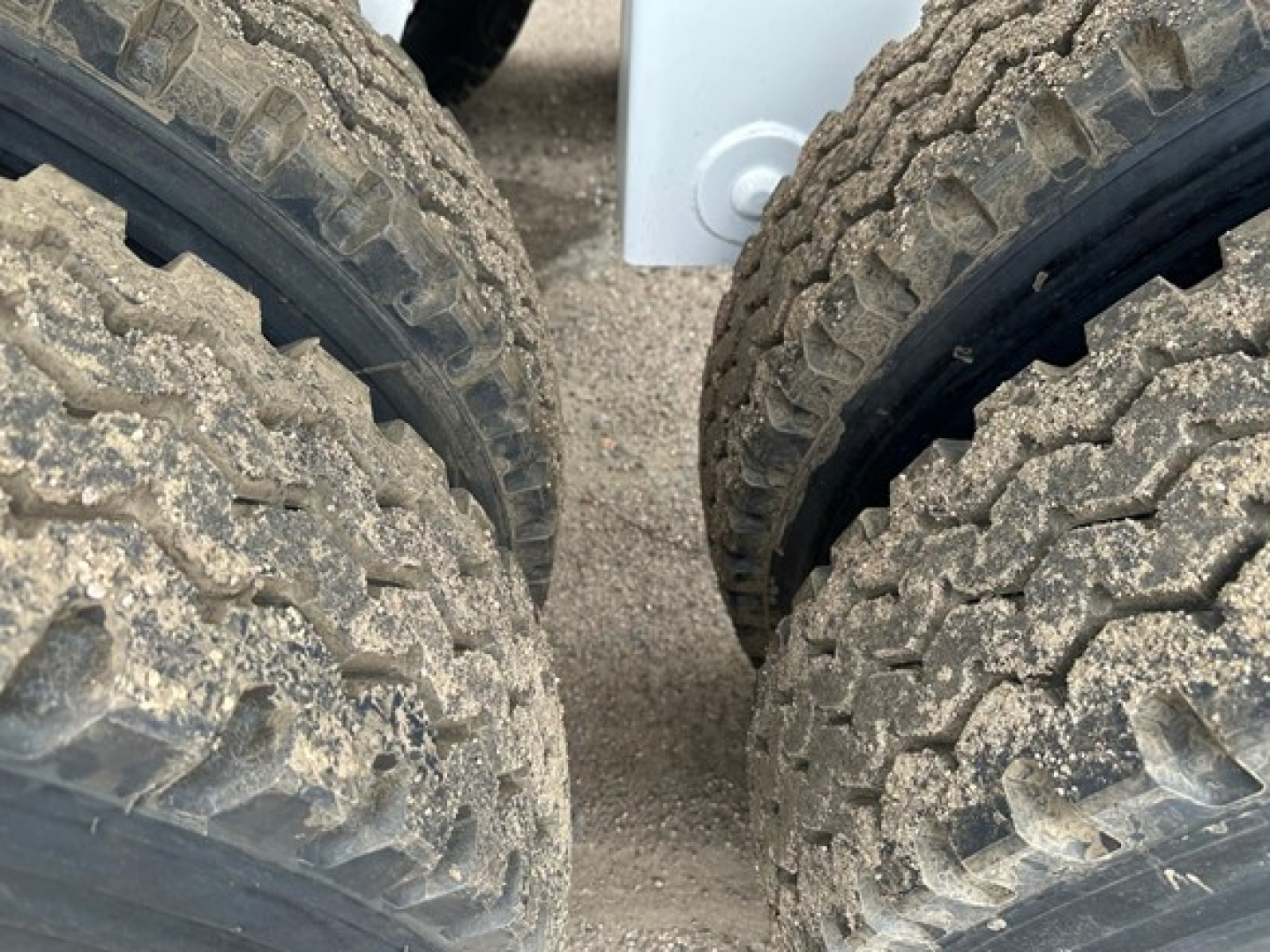 Dump trailer axle tires with rugged tread viewed from between wheels, showing dirty dual tires and partial frame.