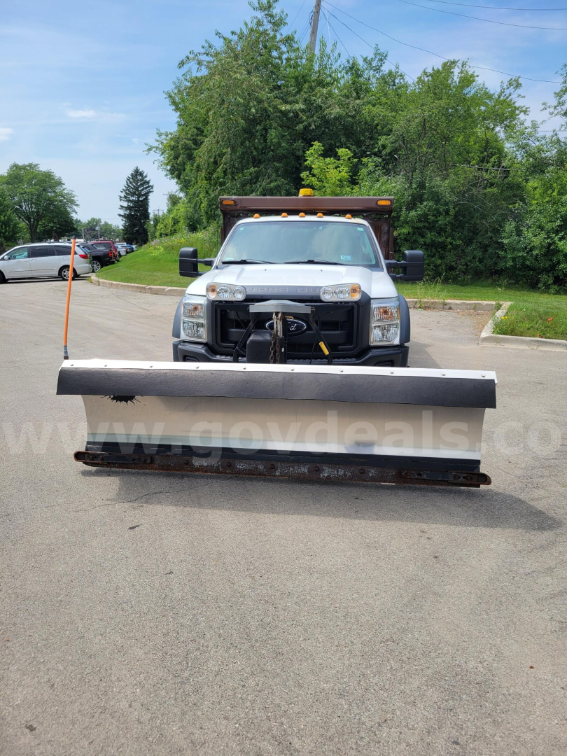 Front view of a white 2012 Ford F-550 with snow plow attachment, headlights, grille, and towing hitch visible.