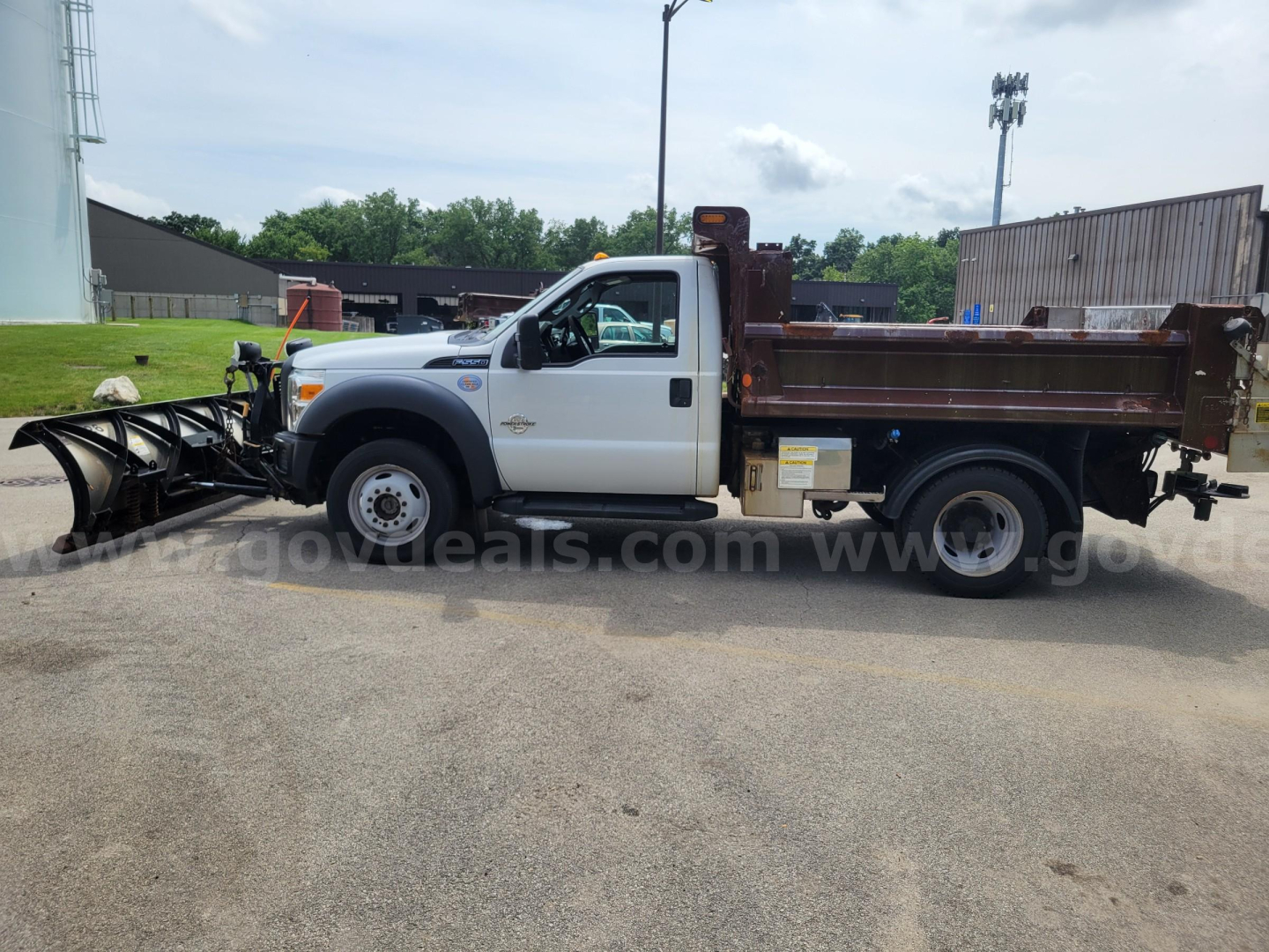 Ford F-550 dump truck with front plow attachment, side view showing white cab and brown dump bed, van with decals, stock number not visible.
