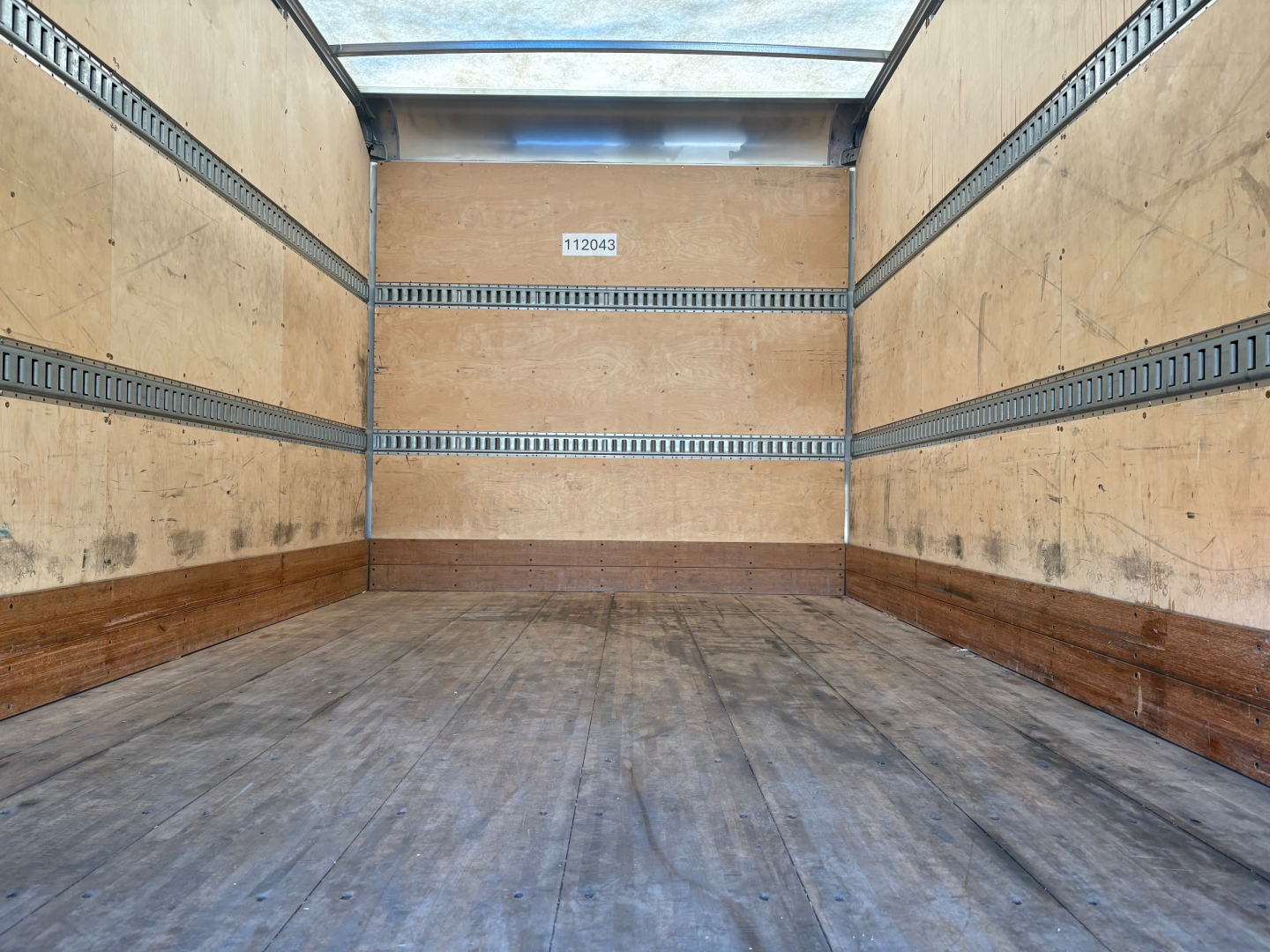 Truck box interior showing empty cargo space with wooden sidewalls and metal E-track rails.