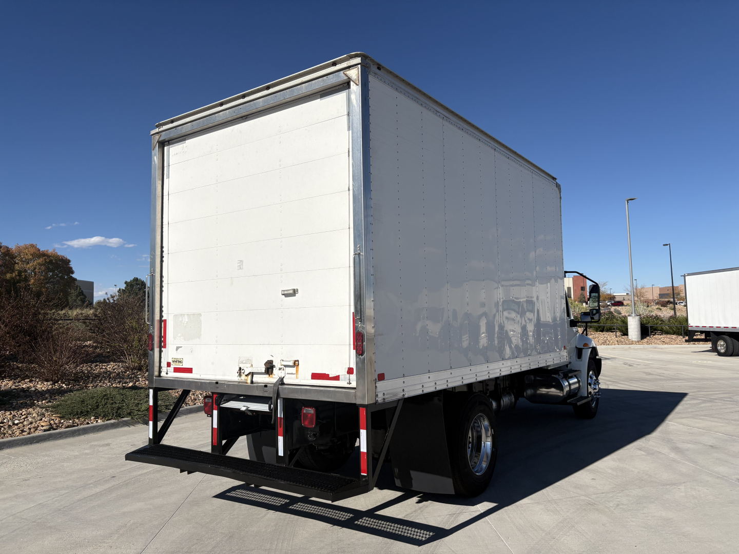 Box truck with white cargo box viewed from rear-right showing back doors and bumper rails.
