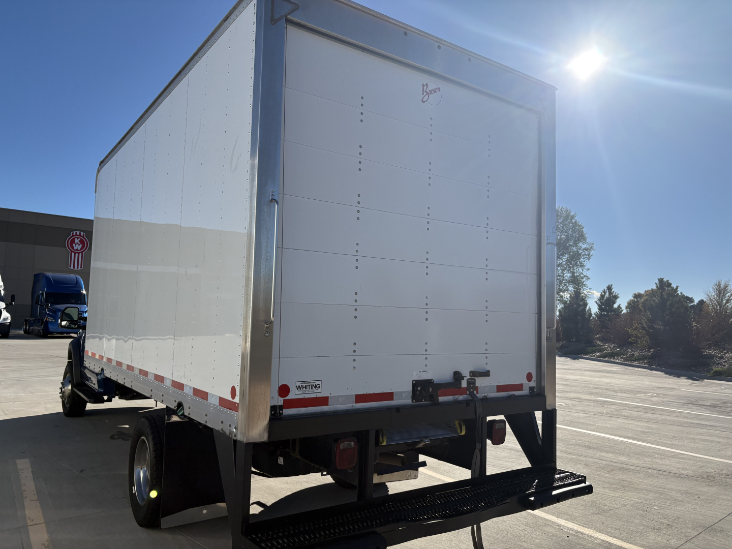 Box truck rear view showing large white roll-up door and bumper with reflective tape.