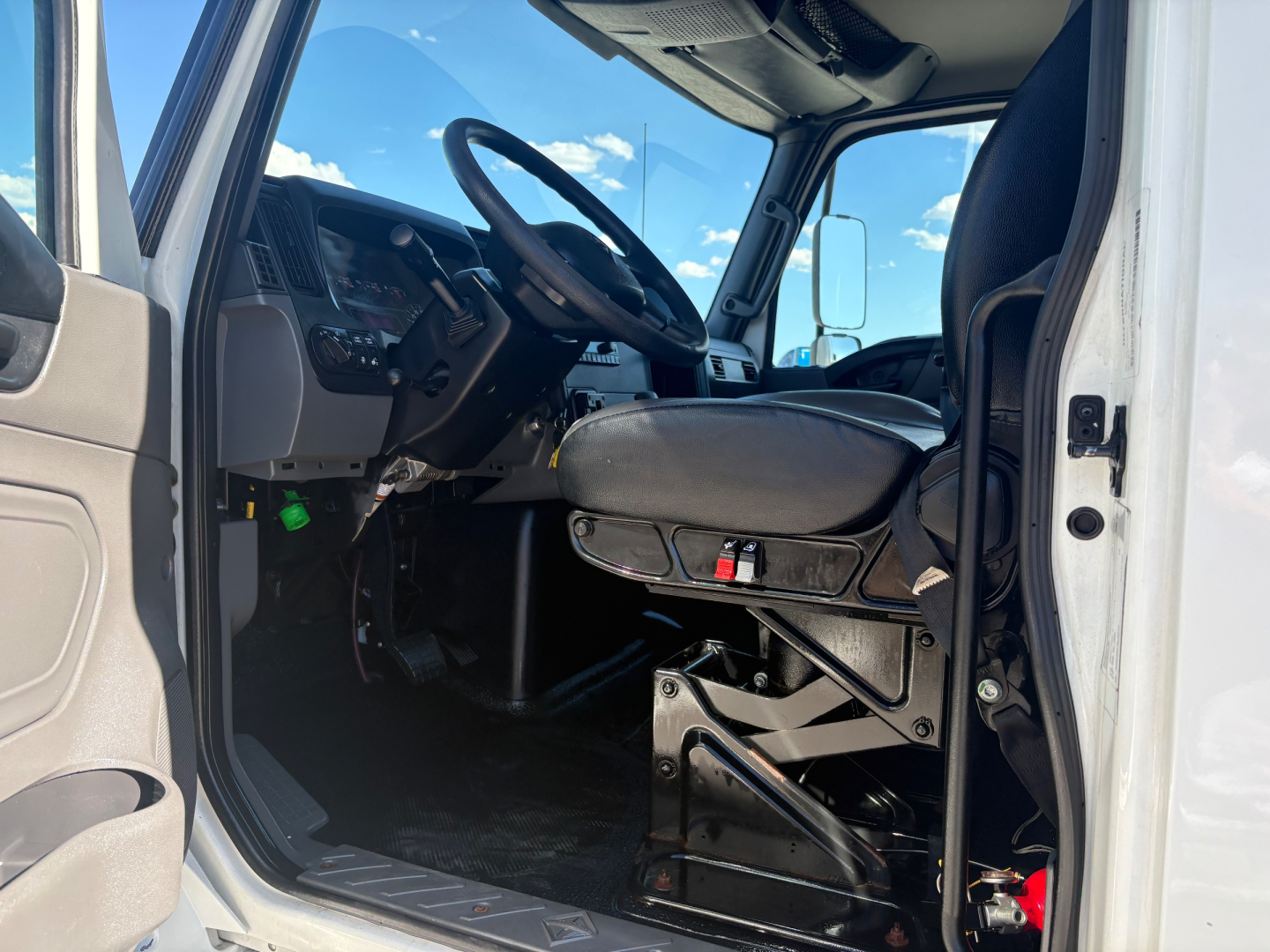 Truck cab interior of a 2021 International MV607 showing driver seat, steering wheel, dashboard, and entry area.