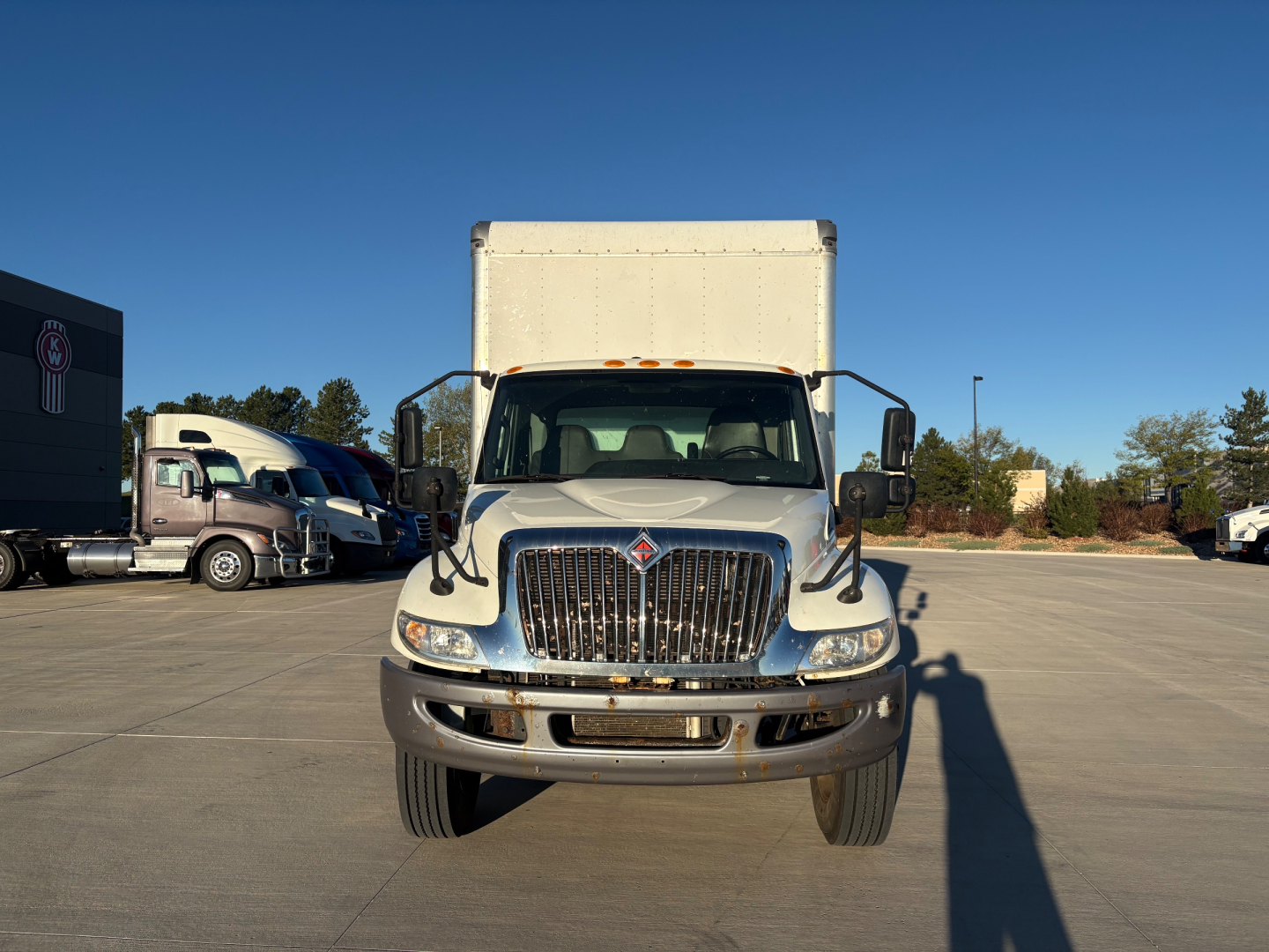 Truck front view of 2021 International MV607 box truck showing grille, headlights, and cargo box; clear sky and dealership lot in background.