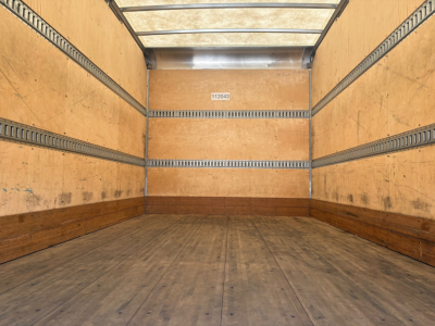 Truck box interior showing wooden walls and floor with metal E-track rails along the sides and a small label on the back wall.