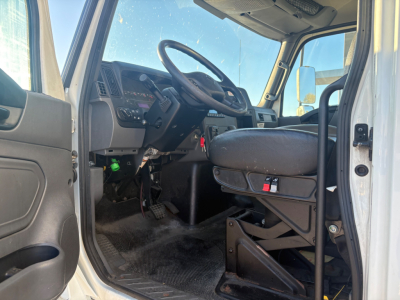 Cab interior of a 2021 International MV607 box truck showing steering wheel, driver seat, dashboard, pedals, and entry area.