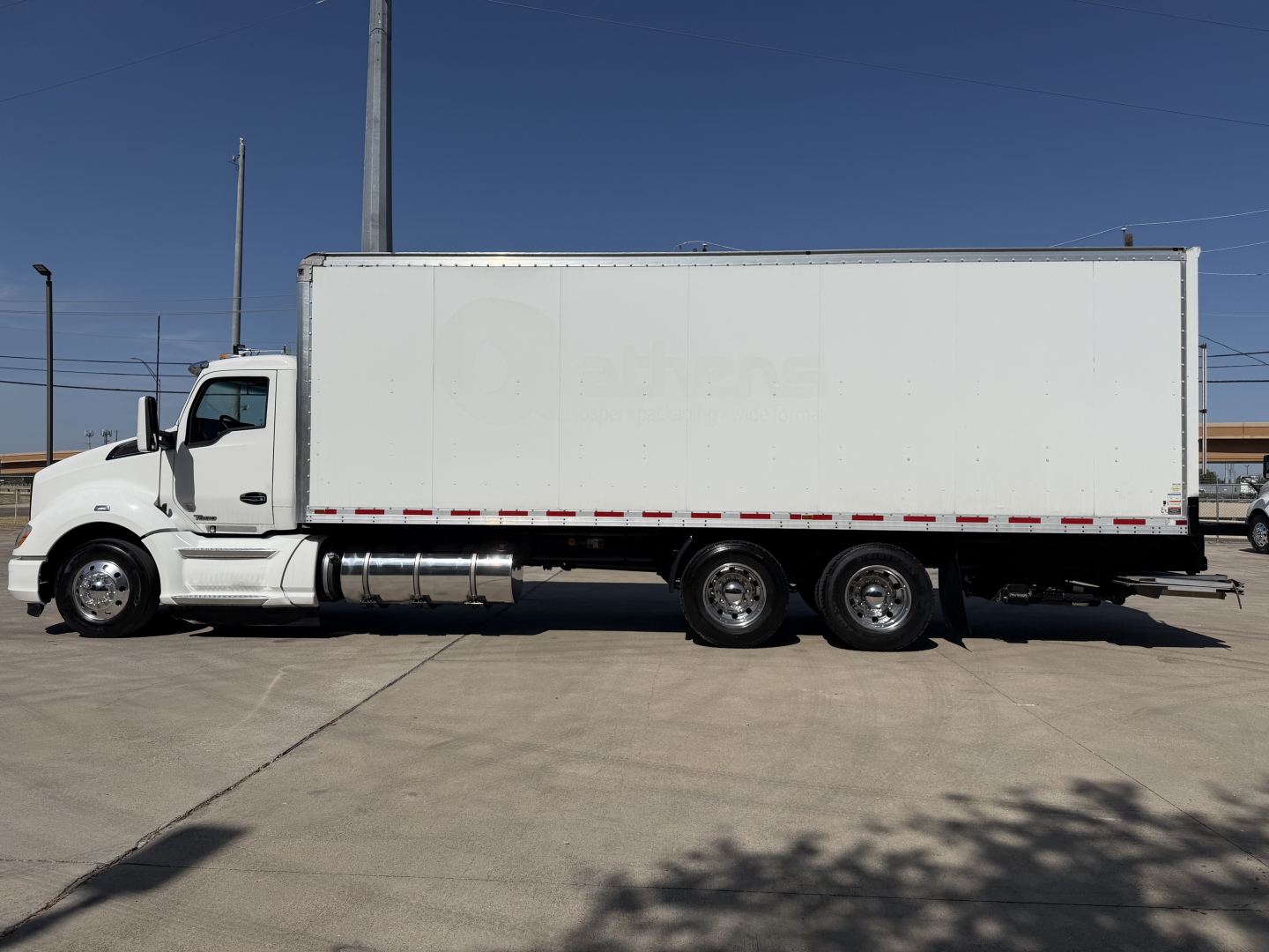 Kenworth T680 box truck side view showing white cargo box and cab with triple rear axles.