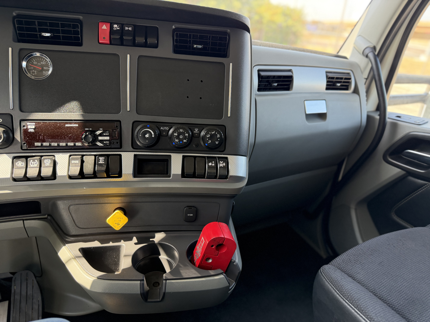 Kenworth T680 dash area showing gauges, vents, controls, cup holder, and a red anti-theft steering wheel lock in the cabin.