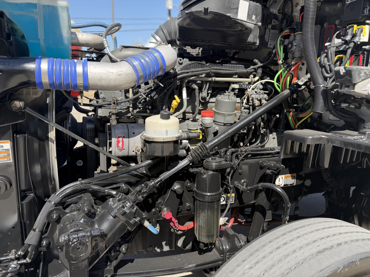 Kenworth T680 engine bay showing air intake, hoses, and wiring harnesses with various fluid reservoirs and components visible.