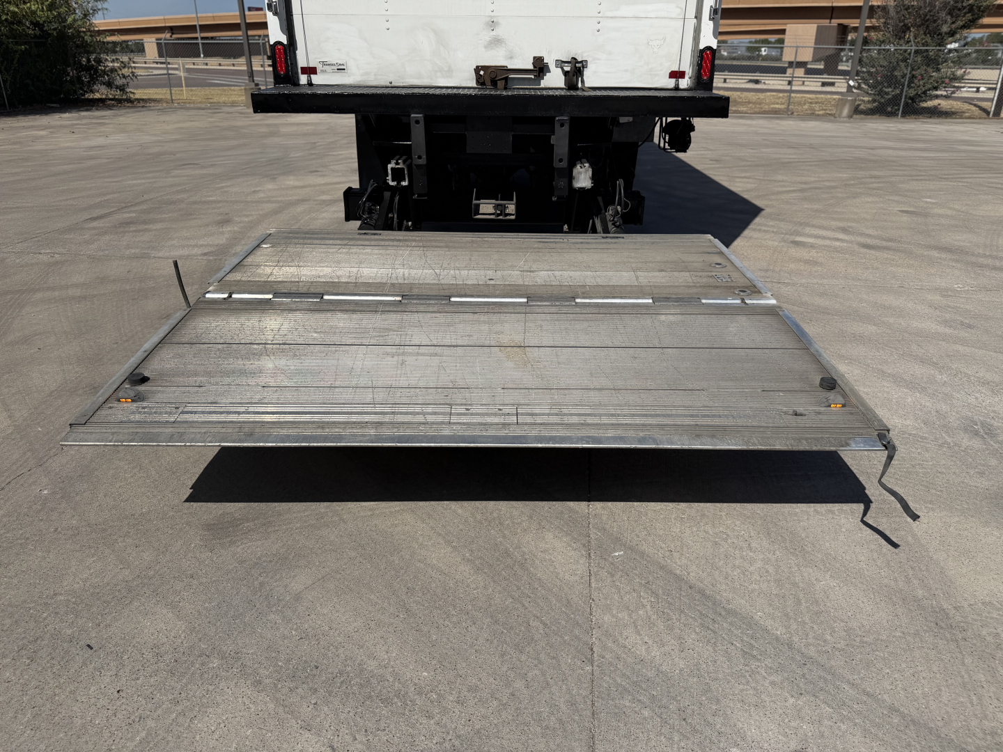Back of a Kenworth T680 with a metal fold-down liftgate extending outward from the truck bed.