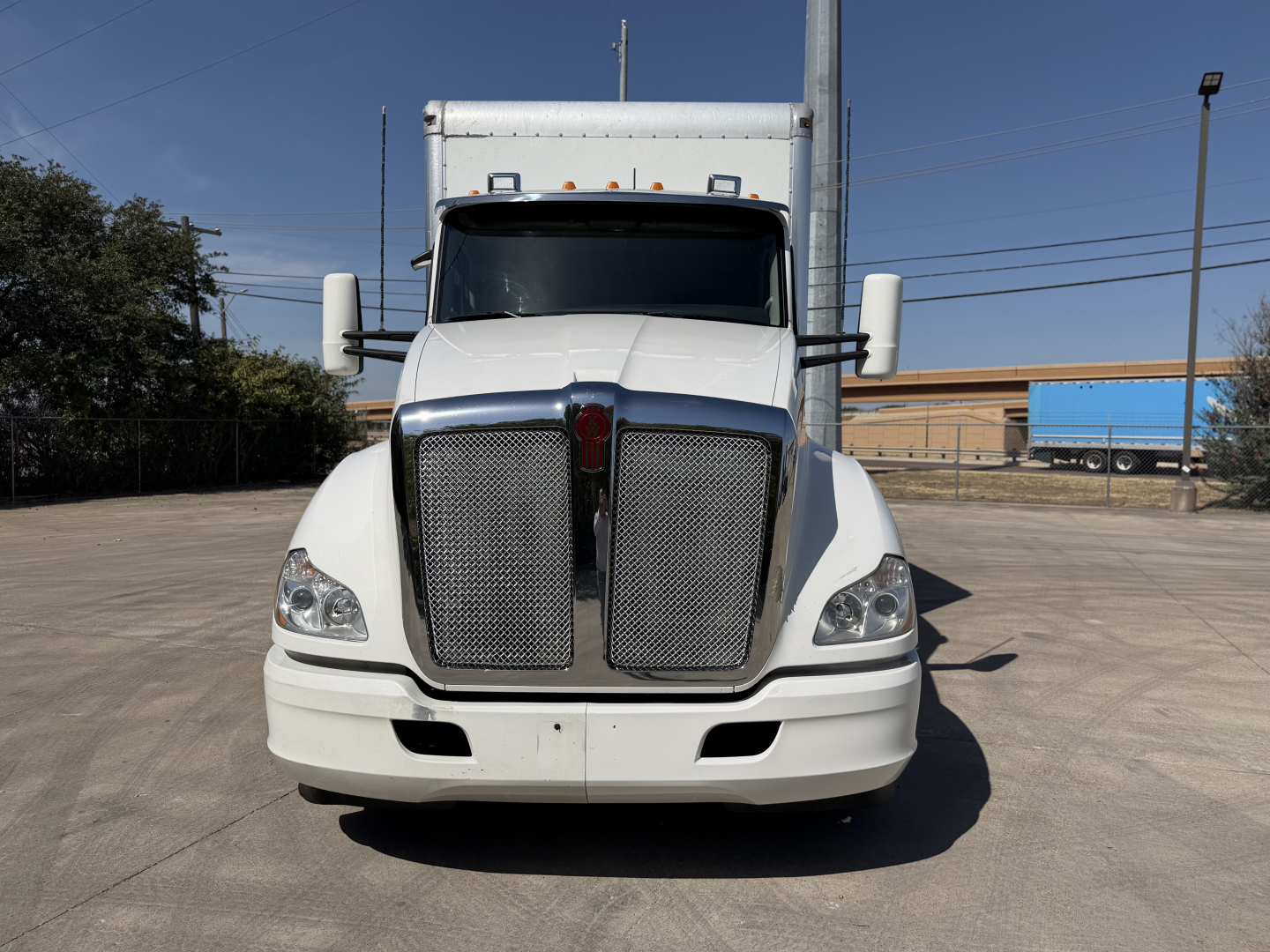 Kenworth T680 box truck front view showing chrome grille, white cab, large side mirrors, and headlights.