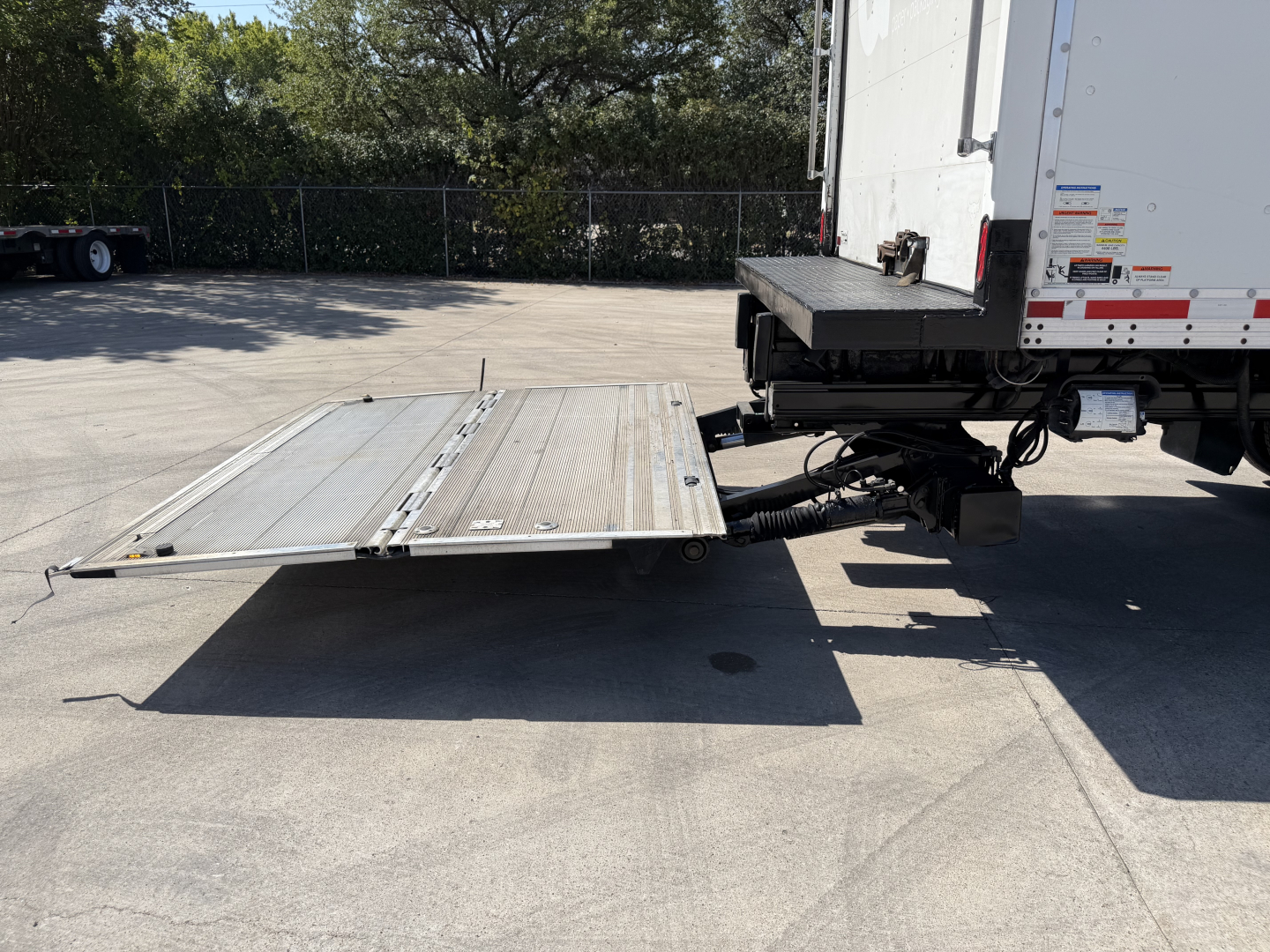 Kenworth T680 with fold-down aluminum loading ramp extended from rear of truck box, view of hitch and undercarriage.