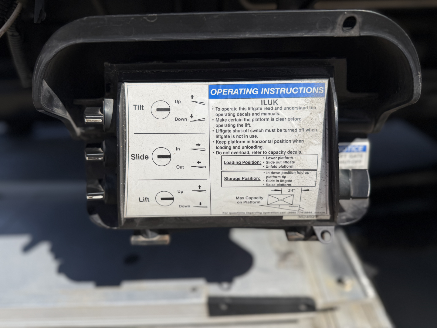 Tow hitch control unit with operating instructions label showing tilt/slide/lift directions and up/down arrows, plus a blue 'OPERATING INSTRUCTIONS' header and small print text.