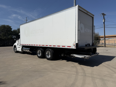Kenworth T680 truck with a large box trailer, rear view showing back doors and triple rear axles.