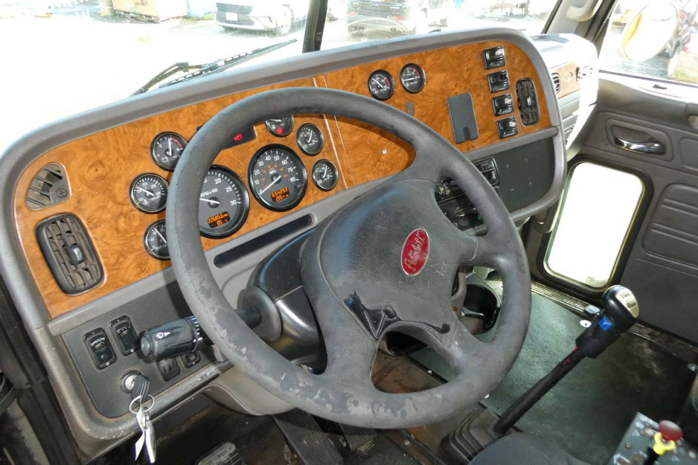 Peterbilt truck cabin interior with woodgrain dashboard, multiple gauges, steering wheel, and gear shifter visible.