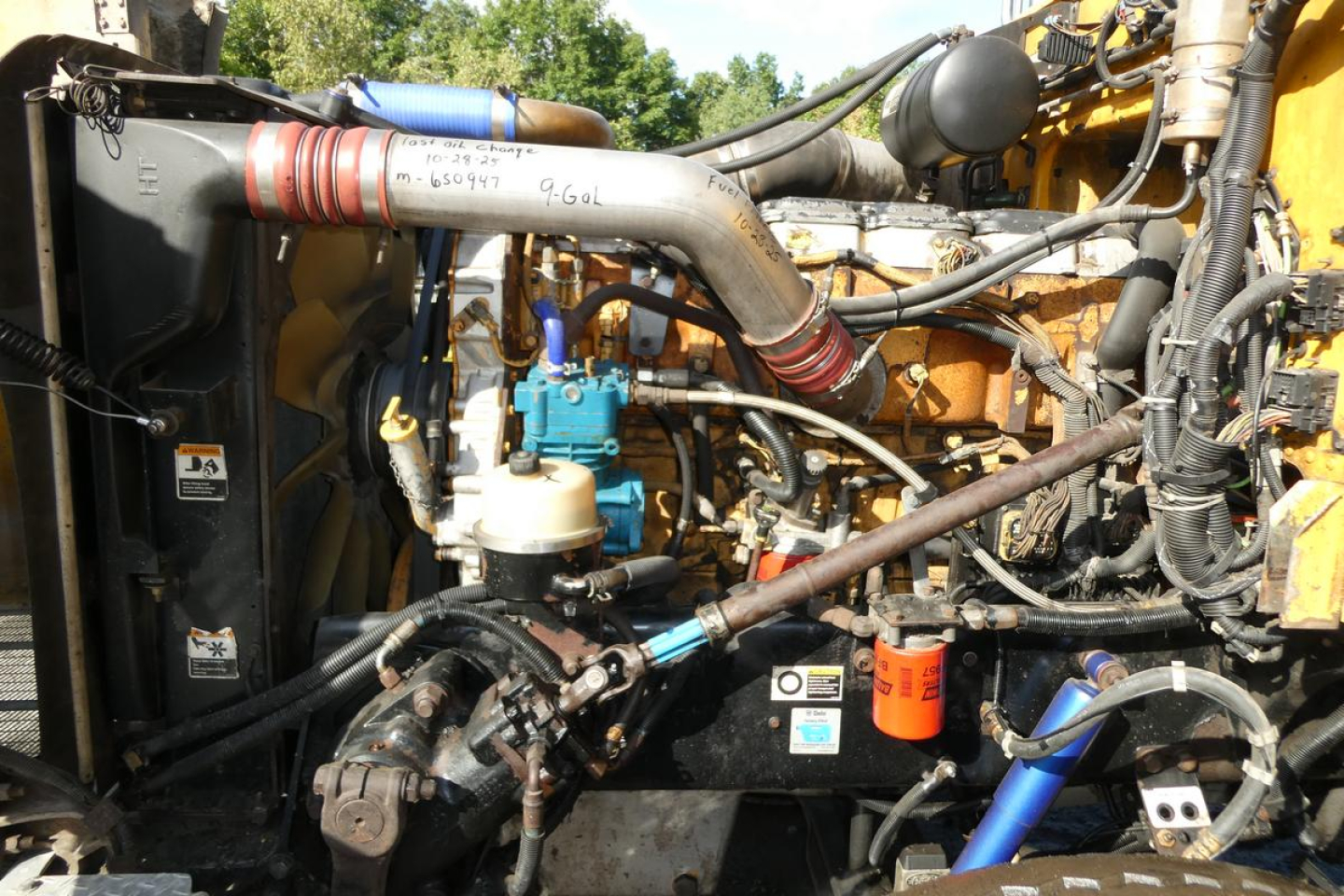 Peterbilt truck engine bay showing large intake manifold, blue fuel filter, hoses, and yellow chassis components.