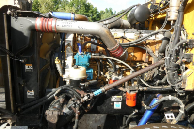 Peterbilt truck engine bay showing large intake manifold, blue fuel filter, hoses, and yellow chassis components.