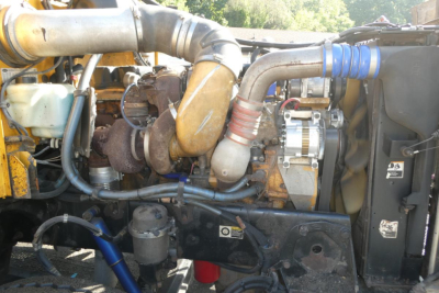 Peterbilt engine bay showing turbocharger, coolant reservoir, hoses, and wiring in diesel truck engine compartment.
