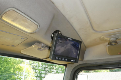 Cab interior with a small in-cab monitor mounted above windshield showing rear view; overhead console lights visible; part of Peterbilt 357 dump truck interior.