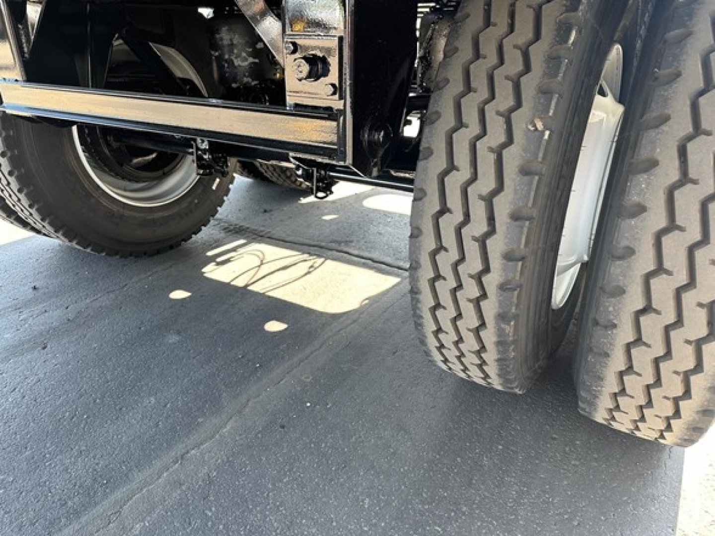 Dual rear tires of a Jet Side Dump trailer with chrome undercarriage and shadowed wheel wells.