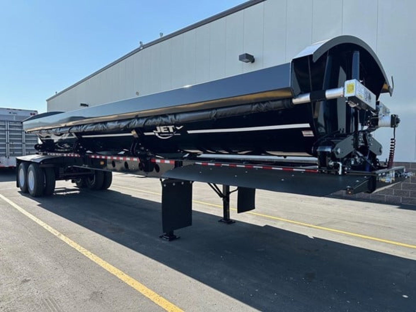 Jet side dump trailer in service view showing long black body with brand name Jet and rear stabilizer legs.