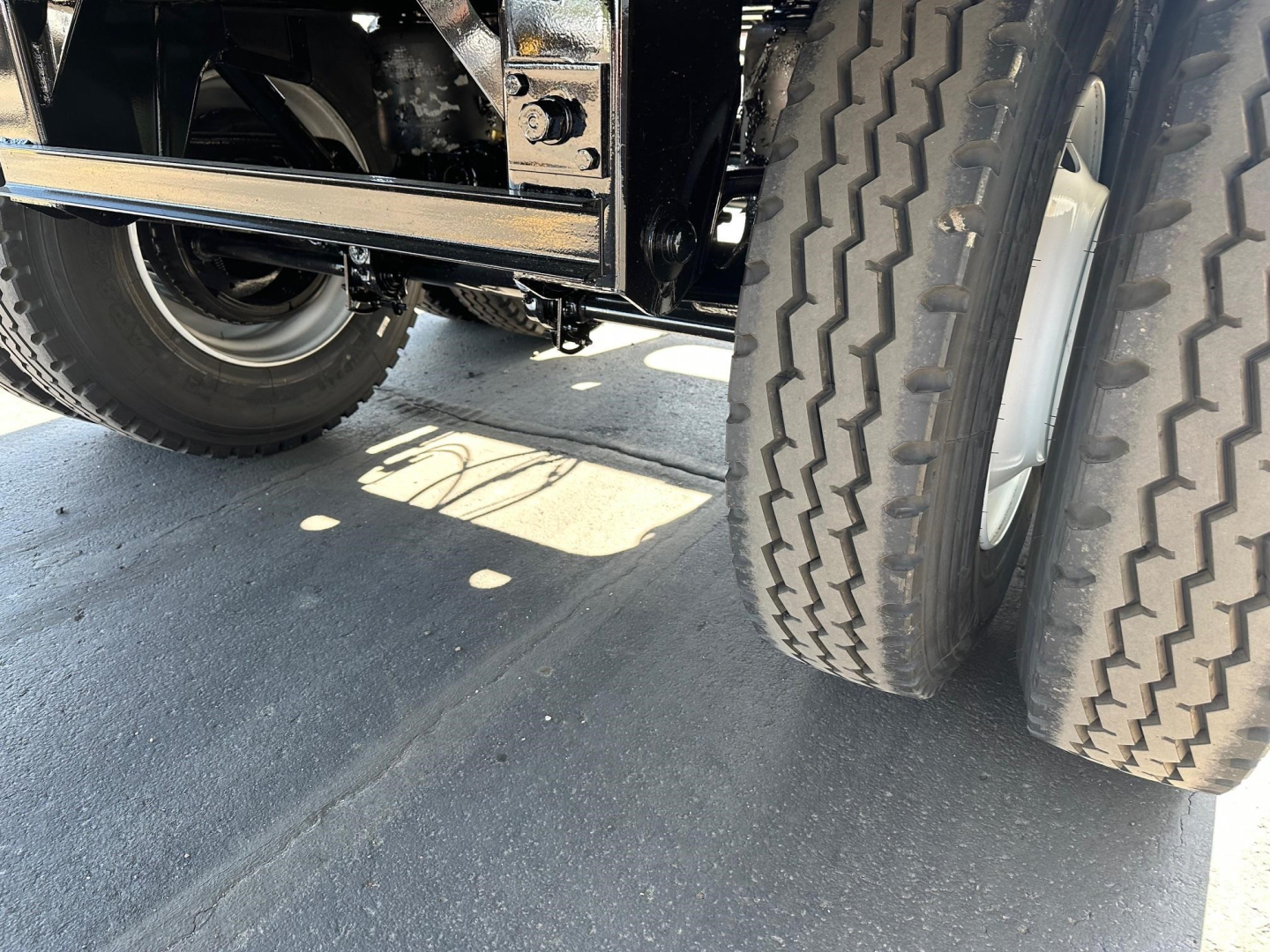 Dual rear tires of a trailer chassis with black painted frame and undercarriage components visible.