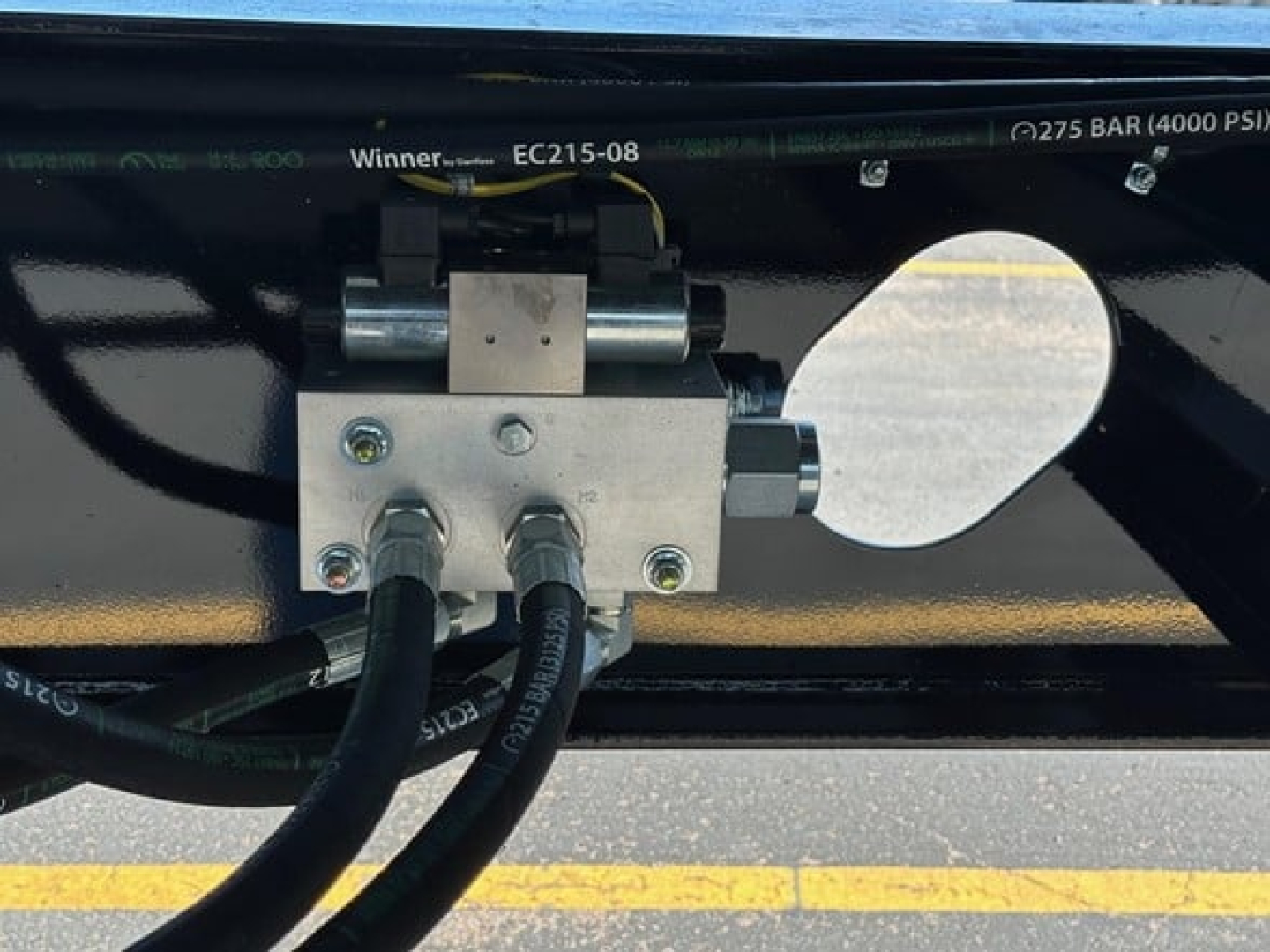 Panel with hydraulic valves and hoses mounted on the underside of a Jet Side Dump trailer showing a metal block with two hoses and a lever/valve assembly.