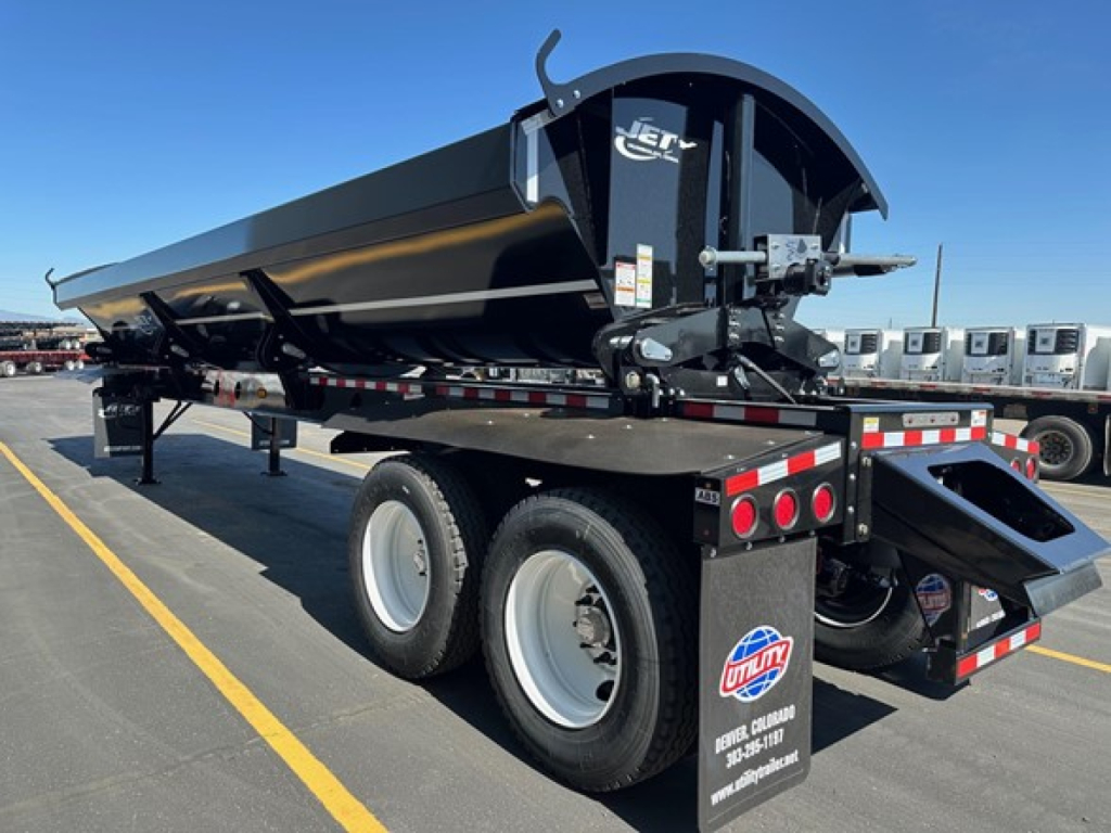 Jet side dump trailer showing black dump body with undercarriage and dual rear axles; side view highlights hydraulic dump mechanism and rear mud flaps.