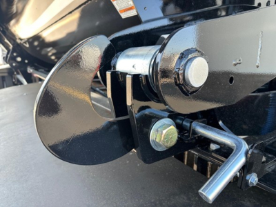 Front end of a jet side dump trailer showing a black pivot arm and bolt with a silver pin and a curved chrome blade.