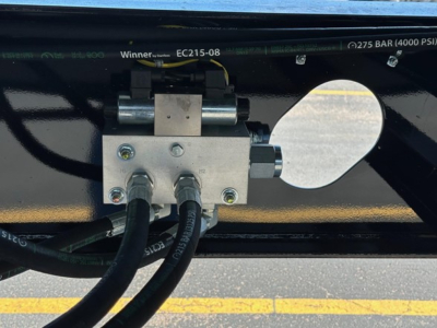 Trailer hydraulic control block with three hoses and mounting plate; various stamped numbers and bar pressure labels along top edge.
