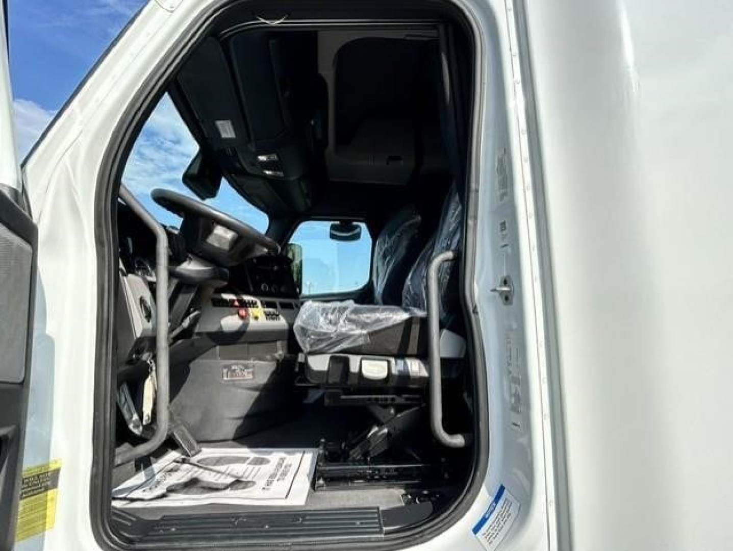 Truck cab interior of a 2021 Freightliner Cascadia 126 with driver seat and dashboard visible through open door.
