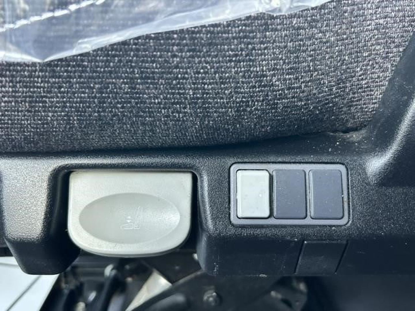 Truck interior detail showing a 12V auxiliary power outlet cap and three small rectangular switches near a control panel in a Freightliner Cascadia dash area.
