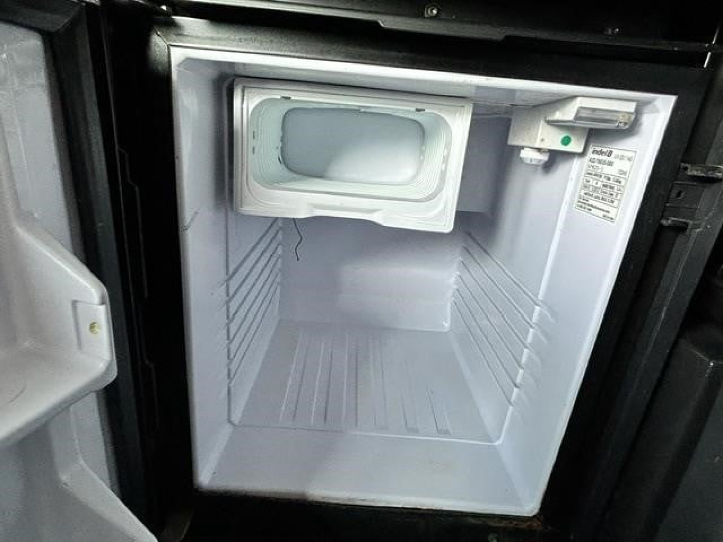 Freightliner Cascadia engine bay showing compact auxiliary cooler or starter area? image appears to show a small front storage compartment or auxiliary unit in a recessed bay with a white interior and label on right side.