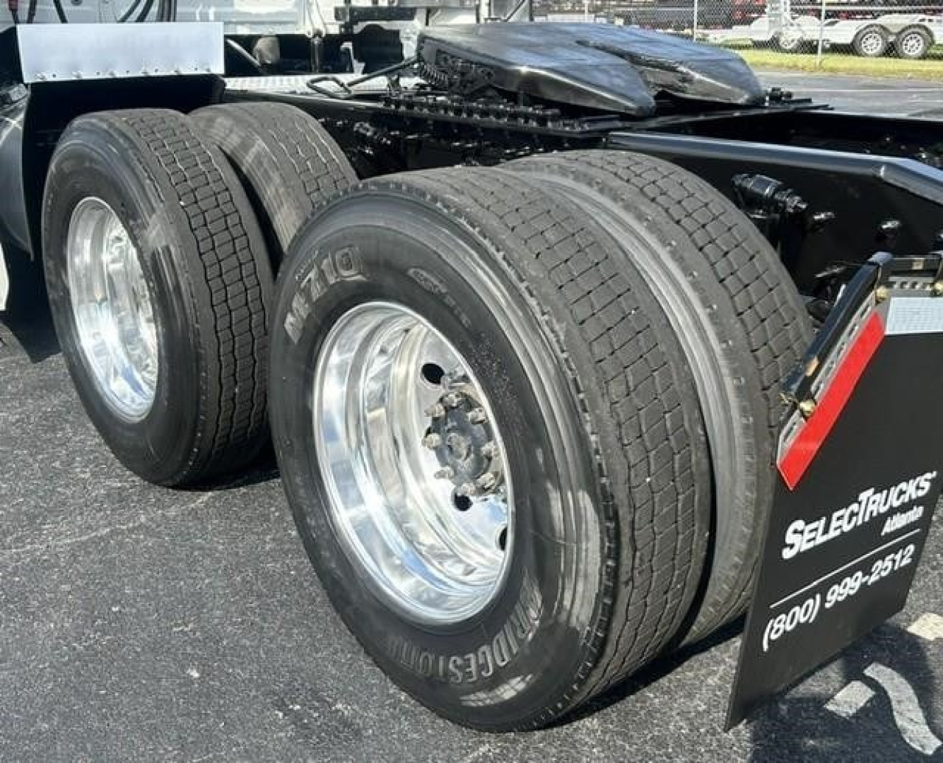 Dual rear axle on a Freightliner Cascadia truck showing heavy-duty tires and chrome rims; part of the chassis and fifth-wheel deck visible.