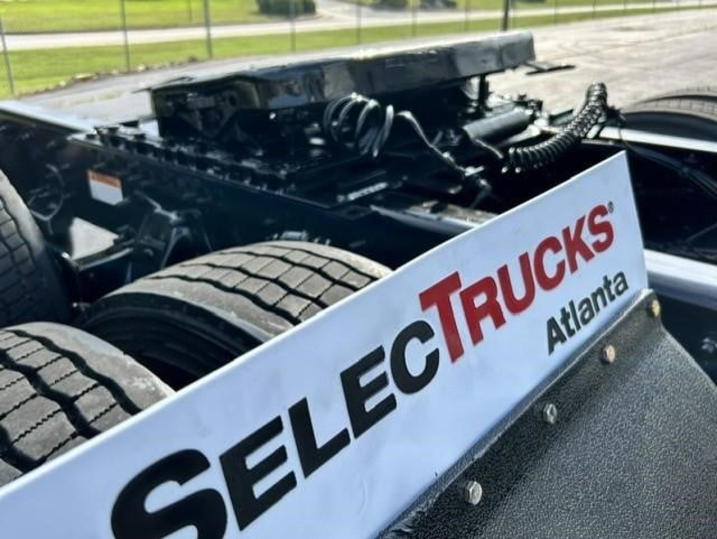 Truck chassis with heavy-duty frame and wheel, Freightliner Cascadia sleeper cab undercarriage visible, Select Trucks Atl logo panel in foreground.