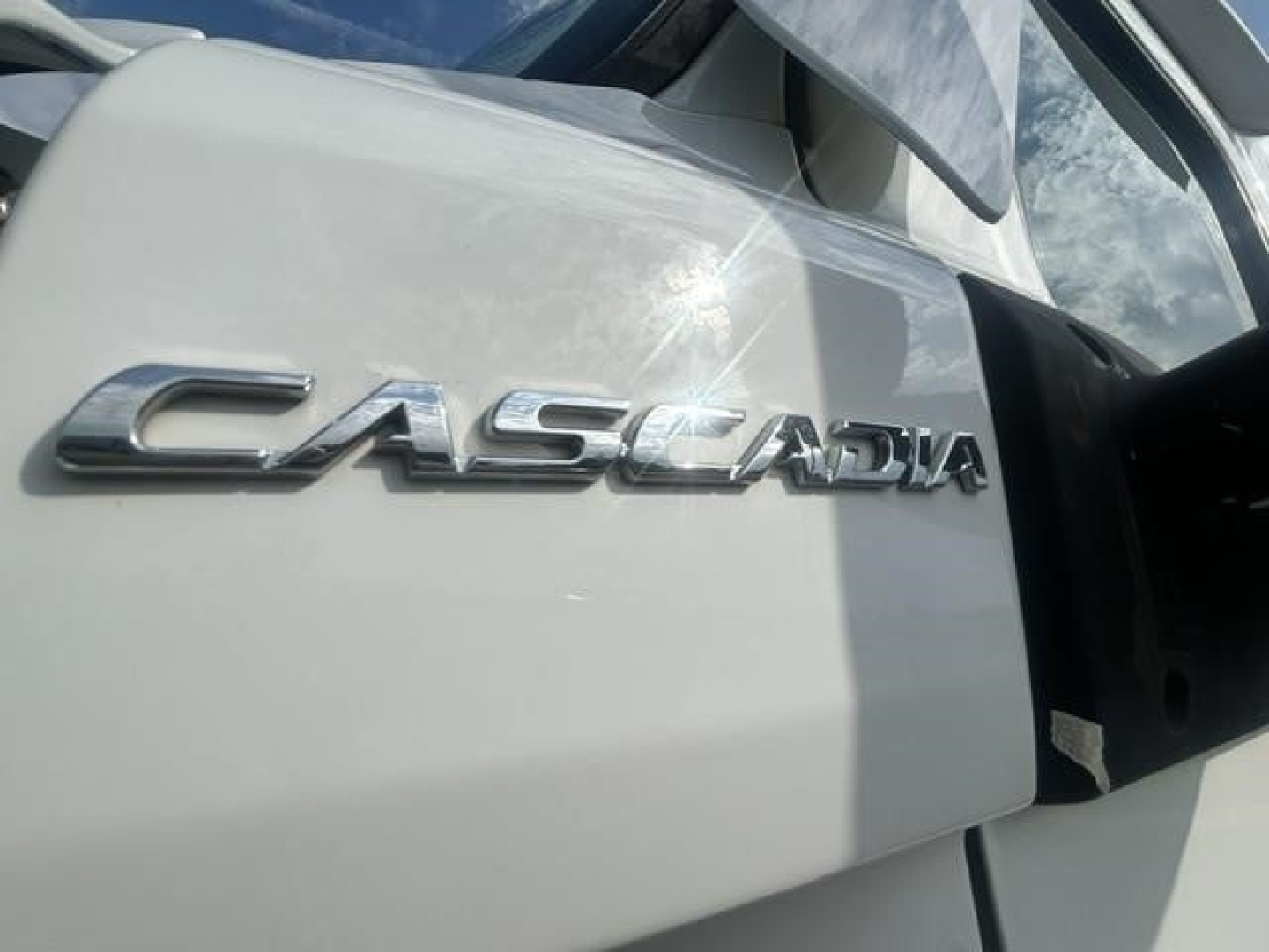 Freightliner Cascadia emblem on cab door showing 'CASCADIA' chrome badge with part of the door and window.