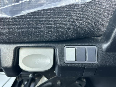Truck interior detail showing a 12V auxiliary power outlet cap and three small rectangular switches near a control panel in a Freightliner Cascadia dash area.