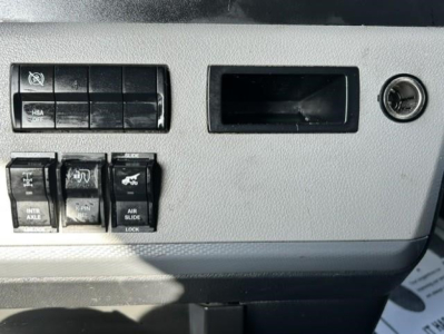 Freightliner Cascadia dash panel showing switches and blank slot; ignition barrel to right; multiple rocker switches labeled INTR AXLE, SLIDE, AIR SLIDE, and other controls.