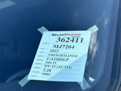 Vehicle tag on windshield with stock number 362411, label shows 2023 Freightliner model CA126SLP, engine DD-15, DT-12 (AUTO), R. AXLE 2.28, VIN MJ7204, etc.