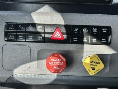 Dashboard control panel of a Freightliner Cascadia showing various switches including hazard, parking brake, and trailer supply red cap labeled 'TRAILER SUPPLY' along with 'PARKING BRAKE' yellow cap.