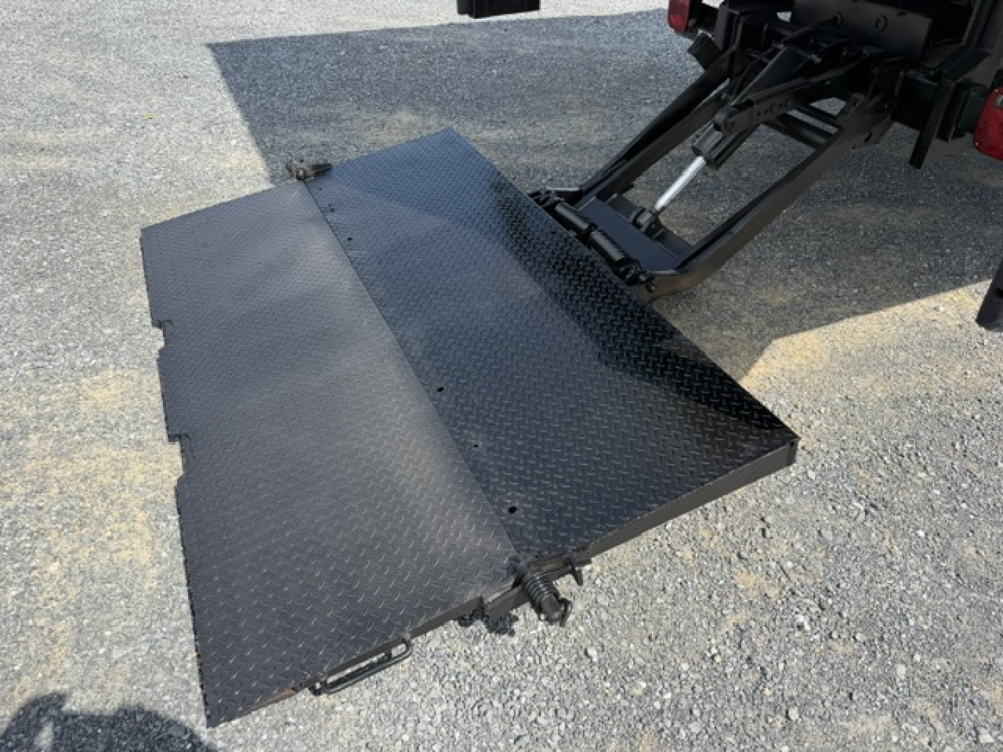 Flatbed platform and hydraulic ramps of a Ford F-750SD truck viewed from rear, showing Diamond-plate steel surface and loading ramp at tail.