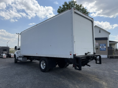 Ford F-750SD box truck rear/side view showing a large rectangular cargo box on dual rear wheels, with a white tailgate. No visible text legible on the truck; surroundings show a dealership lot.