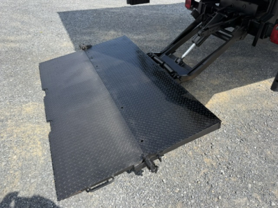 Flatbed platform and hydraulic ramps of a Ford F-750SD truck viewed from rear, showing Diamond-plate steel surface and loading ramp at tail.