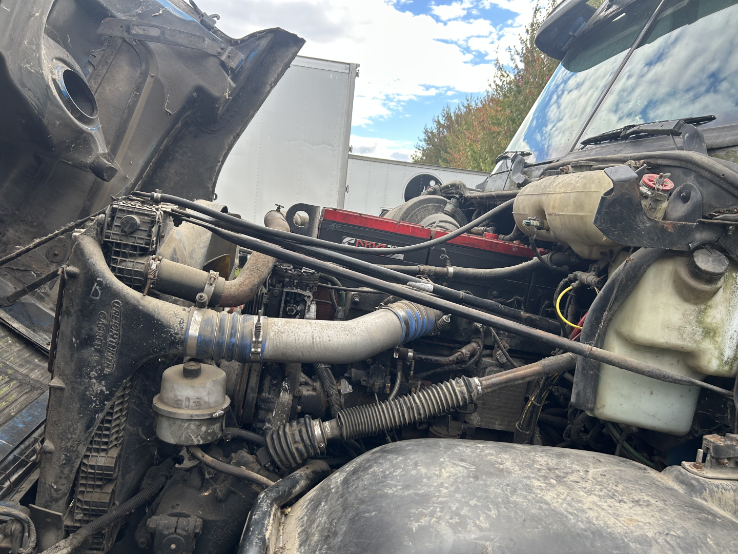 Truck engine bay in a Freightliner FC2, showing hoses, reservoir, and various components under the hood.