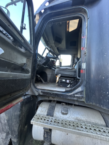 Truck cab interior of a used 1999 Freightliner FC2, driver seat visible through open door, entry step and exterior grime on lower cab area.
