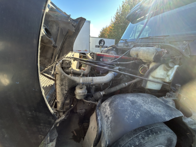 Engine bay of a Freightliner FC2 truck showing exposed hoses and components with a dusty air intake in view.