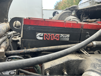 Battery area of a Freightliner FC2 engine bay showing Cummins N14 Plus badge and surrounding hoses and components.